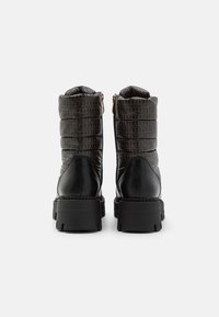 Bottes à cheville noires matelassées avec un bout et un talon en cuir noir brillant, dotées d'une fermeture éclair sur le côté et d'une semelle en caoutchouc épaisse. Design de dessus texturé.