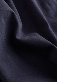 Marinblå bomullstyg, mjuk textur med en lätt glans, med släta, jämna stickmönster och mjuka veck.
