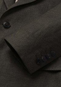Ärmel eines strukturierten dunkelolivgrünen Anzugsakts mit vier schwarzen Knöpfen und einem Teil der Vorderseite mit einem schwarzen Knopf sichtbar.