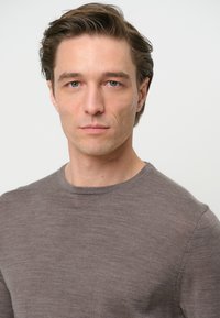 Maglione grigio a collo rotondo con una texture liscia, caratterizzato da un design aderente e dettagli di cucitura sottili, indossato da un uomo con i capelli corti.