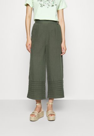 Grønne hørbukser med vide ben og syninger nær kanten, kombineret med beige platformsandaler med flere remme.