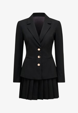 Musta räätälöity bleiseri, jossa on kolme kullanväristä nappia, yhdistettynä vastaavaan mustaan laskostettuun hameeseen, yhdistettynä yhtenäiseksi asukokonaisuudeksi.