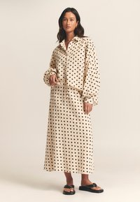 Beige polka dot shirt and matching skirt set in a soft fabric. Shirt features a collar and button closure; skirt is long and flowy.