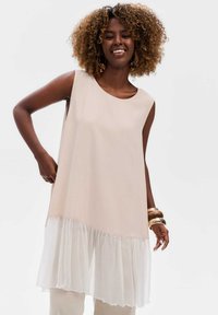 Mouwloze nude tuniek met een vloeiende witte gelaagde zoom. Lichtgewicht stof met een relaxte pasvorm, kenmerken zijn een ronde halslijn en afgeronde randen.