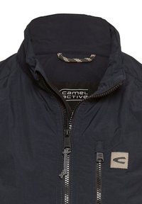 Marineblaue Jacke mit Stehkragen, durchgehendem Reißverschluss, kontrastierenden Reißverschlussdetails und einem Stoffetikett mit Logo auf der Vorderseite.