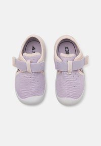 Zapatos de rejilla en lavanda claro con suela de goma blanca y correa ajustable. Presentan una punta redondeada y un cuello acolchado para mayor comodidad.
