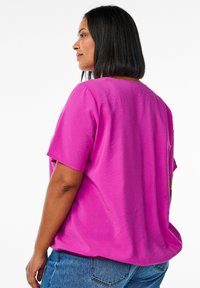 Top fucsia a maniche corte realizzato in un materiale liscio, con una vestibilità comoda e un collo rotondo, abbinato a jeans in denim blu.