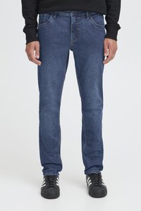 Mörkblå denimjeans med rak passform, utrustade med fem fickor och knäppning med knapp. Bärs med svarta sportskor.