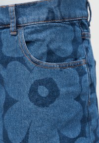 Τσέπη τζιν με σκούρο μπλε λουλουδάτο σχέδιο και πορτοκαλί ραφές, εμφανίζοντας λωρίδα ζώνης και λεπτομέρειες πλαϊνής ραφής.