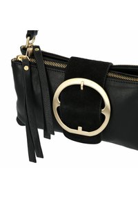 Clutch de cuero negro con cierre de cremallera, con un acento de hardware circular dorado y una correa de ante negro. Acabado texturizado con detalle de flecos.