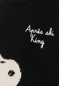 Zwarte gebreide trui met een witte grafische print en de tekst "Après ski King" in cursief. Zachte textuur met geribbelde halslijn.