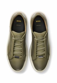Olive green leather sneakers with tonal laces, branding on the tongue, and a white rubber sole featuring a subtle textured detail.