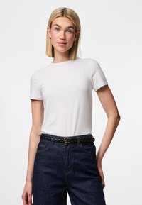 Hvit bomulls-T-skjorte med korte ermer og rund hals, brukt med mørk denim, utstyrt med et flettet svart belte. Enkel og tettsittende design.