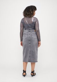 Gonna di jeans grigia lunga con tasche posteriori, abbinata a una maglietta aderente e trasparente a maniche lunghe con motivo a macchie di leopardo nero. Tacchi neri.