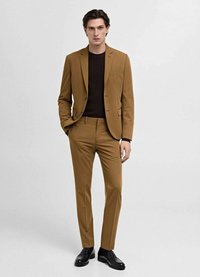 Brown tailored suit with notch lapels, slim fit trousers, and a textured dark sweater. Black leather shoes complete the outfit.