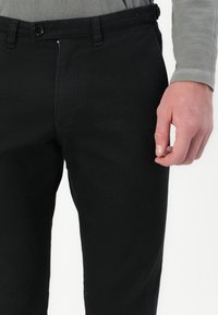 Svarta jeans har en slim fit, klassisk femfickdesign, knäppning med knapp och en mjuk textur, bärs med en grå långärmad skjorta.