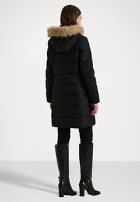 Melnā puffer jaka ar kažokādas apdari kapucei, ar taisnu siluetu, rāvējslēdzēja detaļām un garām piedurknēm. Nēsāta ar melniem zābakiem līdz ceļgaliem.
