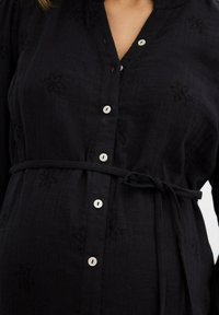 Vestito nero con bottoni, decorato con ricami floreali, dotato di una cintura in vita e bottoni bianchi, realizzato in tessuto testurizzato per una vestibilità comoda.