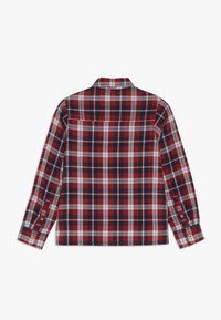 Koszula w kratę w kolorach czerwonym, granatowym i białym, z długim rękawem, zapinanymi na guziki mankietami, kołnierzykiem i pojedynczą kieszenią na plecach. Miękki materiał wkratkę na całej powierzchni.