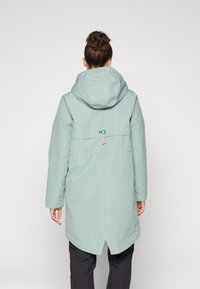 Lichtgroene waterdichte parka met een capuchon, voorzien van een achterzak en een logo. Glad textuur en knielange snit.