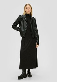 Veste de biker en cuir noir portée sur une robe maxi noire à manches longues. Le mannequin porte des bottes à talons épaisses noires. Texture lisse, design ajusté.