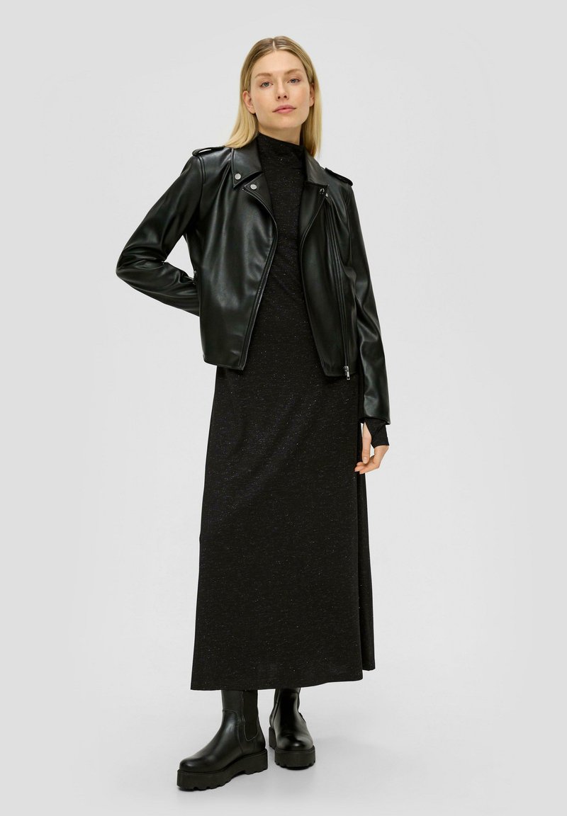 Veste de biker en cuir noir portée sur une robe maxi noire à manches longues. Le mannequin porte des bottes à talons épaisses noires. Texture lisse, design ajusté.