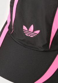 Șapcă neagră cu accente și dungi roz, având un logo Adidas strălucitor în negru și roz pe față. Fabricată dintr-un material neted.