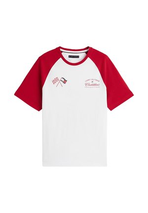 Camiseta blanca con mangas y cuello rojos, con banderas de cuadros cruzadas y texto rojo "Tommy Hilfiger Cadillac Formula 1 Team" en el pecho.