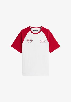 Maglietta bianca con maniche e collo rossi, decorata con bandiere a scacchi incrociate e la scritta rossa "Tommy Hilfiger Cadillac Formula 1 Team" sul petto.