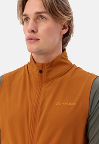Oranges ärmellose Weste mit Reißverschluss und hohem Kragen. Verfügt über ein dezentes Logo und eine Steppnaht. Hergestellt aus leichtem, glattem Material.