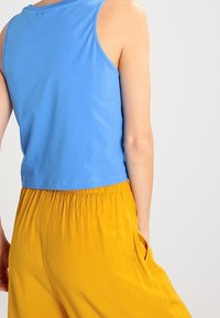 Ljusblå ärmlös croppad topp gjord av bomull, matchad med lösa gula byxor med elastisk midja och sidofickor.