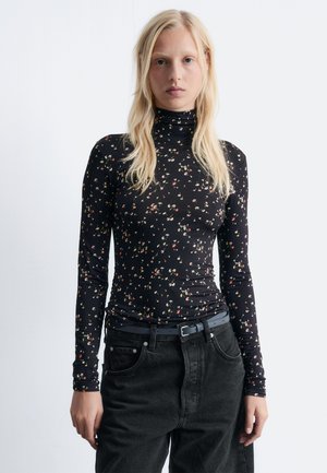 Black long-sleeve turtleneck with a floral pattern in red, yellow, and green. Soft, stretchy fabric paired with high-waisted black pants.