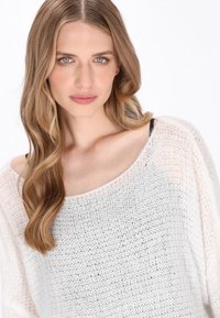 Biały, luźno dziergany sweter z dekoltem typu off-shoulder, z teksturowanym splotem i długimi rękawami. Lekki i przewiewny wygląd.