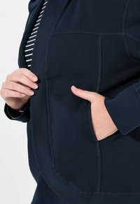 Mörkblå tröja med ribbad textur, med en framficka och ett randigt lager under. Inkluderar synliga sömdetaljer.
