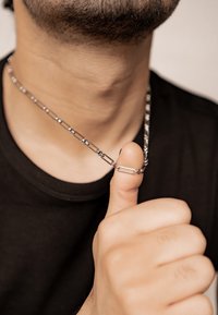 Silver chain necklace with interlocking oval links, resting on a thumb, with a textured finish and a minimalist design.