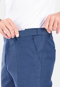 Pantaloni blu su misura con una texture liscia, pence frontali e una vita con passanti per la cintura. Due tasche laterali e una tasca posteriore.