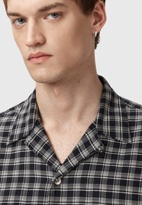 Zwart-wit geblokte shirt met een kraag en knoop. De stof lijkt textuur te hebben met zichtbare stiksels en een relaxed fit.