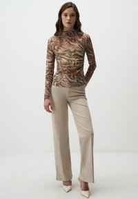 T shirt à manches longues avec un motif zèbre en marron et beige, associé à un pantalon beige coupe droite et des escarpins à bout pointu. Texture lisse.