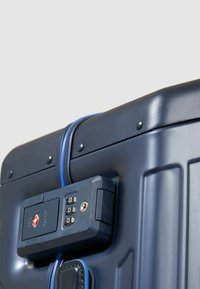 Marineblauer Hartschalenkoffer mit Zahlenschloss, blauem Akzentgurt und strukturierter Oberfläche mit vertikalen Rillen.