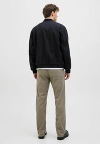 Black bomber jacket with elastic cuffs and hem, paired with light beige trousers and black shoes. Simple design, solid colors, no patterns.