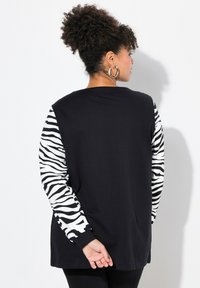Maglietta nera a maniche lunghe con maniche a strisce bianche a zebra, caratterizzata da una vestibilità ampia, scollo rotondo e tessuto morbido. Vista posteriore mostrata.