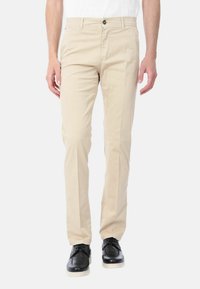 Pantaloni in cotone color beige in stile chino con vestibilità dritta, dotati di chiusura con bottone frontale e tasche laterali. Indossati con scarpe eleganti nere.