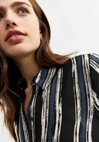 Zwarte shirt met verticale blauwe en witte penseelstrepen, met een kraag en een knopenfront, gemaakt van een zachte stof.