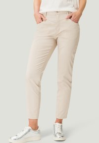Pantalons en mélange coton beige avec une coupe droite, dotés de poches avant et d'une fermeture à bouton, associés à des baskets argentées métalliques.