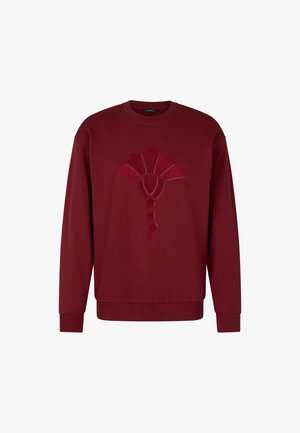 Burgundowa bluza z długim rękawem, z uniesionym, abstrakcyjnym wzorem z przodu. Miękka tkanina z prążkowanymi mankietami i dekoltem.