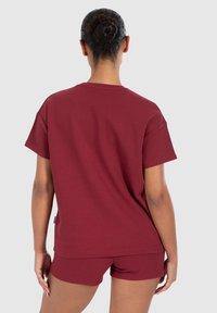T-shirt in cotone bordeaux con vestibilità rilassata e maniche corte, abbinato a pantaloni corti coordinati, che mostrano una finitura testurizzata.