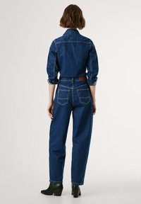 Denimskjorte og høy-midje jeans i mørkeblå. Skjorten har oppbrettede ermer og krage. Jeansene har to baklommer og rette ben.