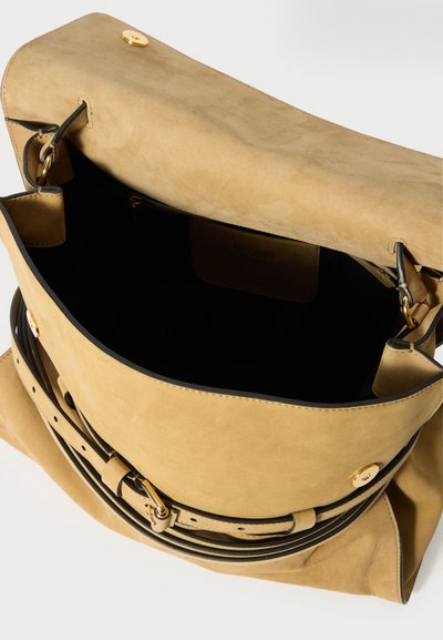 Tan suède schoudertas met gouden gesp en magnetische drukknoop, geopend om de zwarte interieurvoering en het merklabel te onthullen.