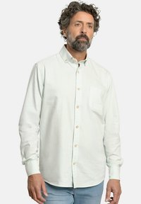 Camisa de manga larga a rayas verde claro con cuello abotonado, que presenta un único bolsillo en el pecho y botones de color marrón claro. Tejido texturizado.