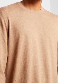 Maglione beige in maglia con scollo tondo, texture liscia e dettagli di cucitura minimi, che mette in luce una forma classica aderente.